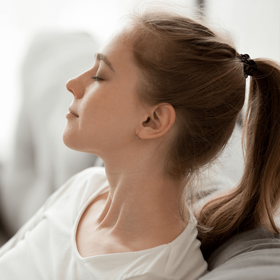 A woman is sitting on a couch with her eyes closed and her hair in a ponytail.