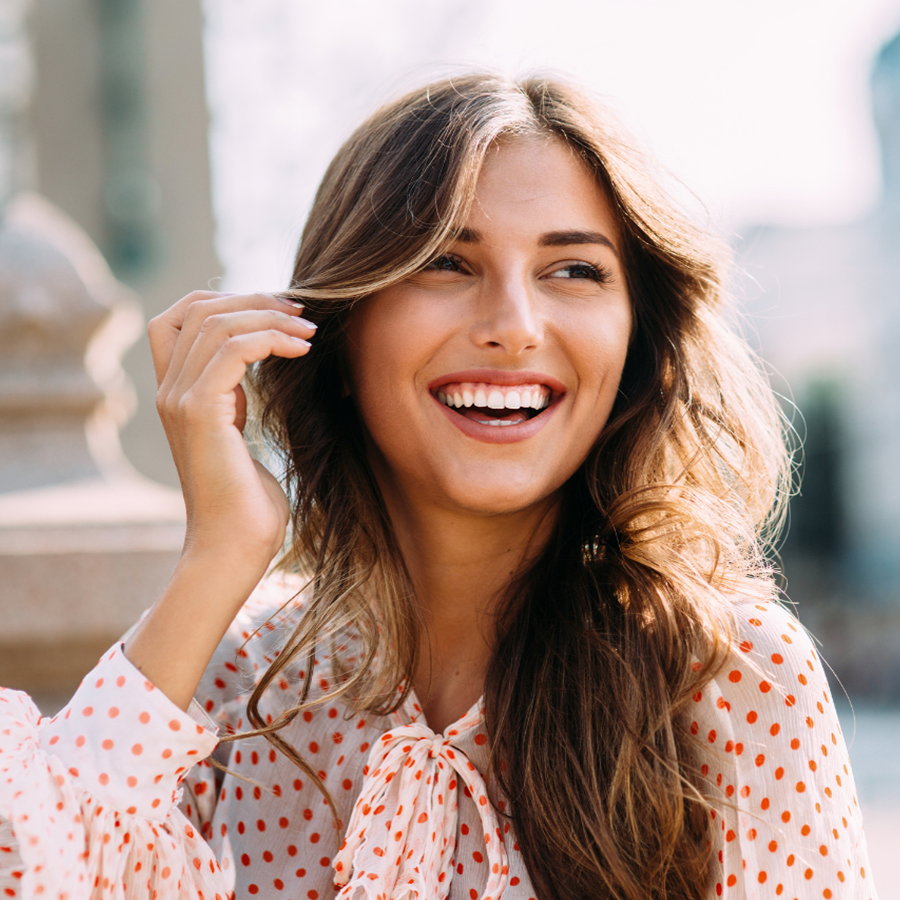 A woman in a polka dot shirt is smiling and touching her hair.