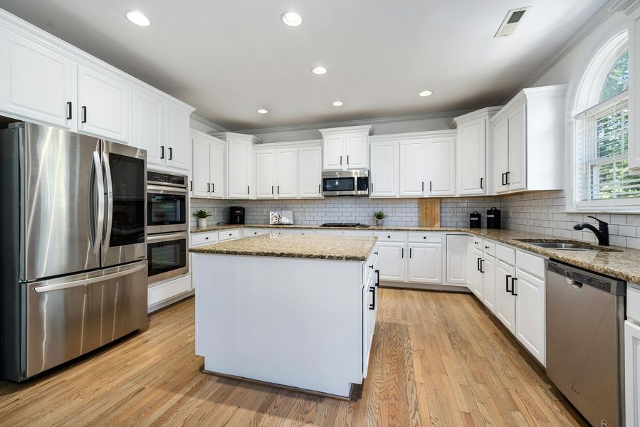 White kitchen with stainless steel appliances, light wood floors, and granite countertops.