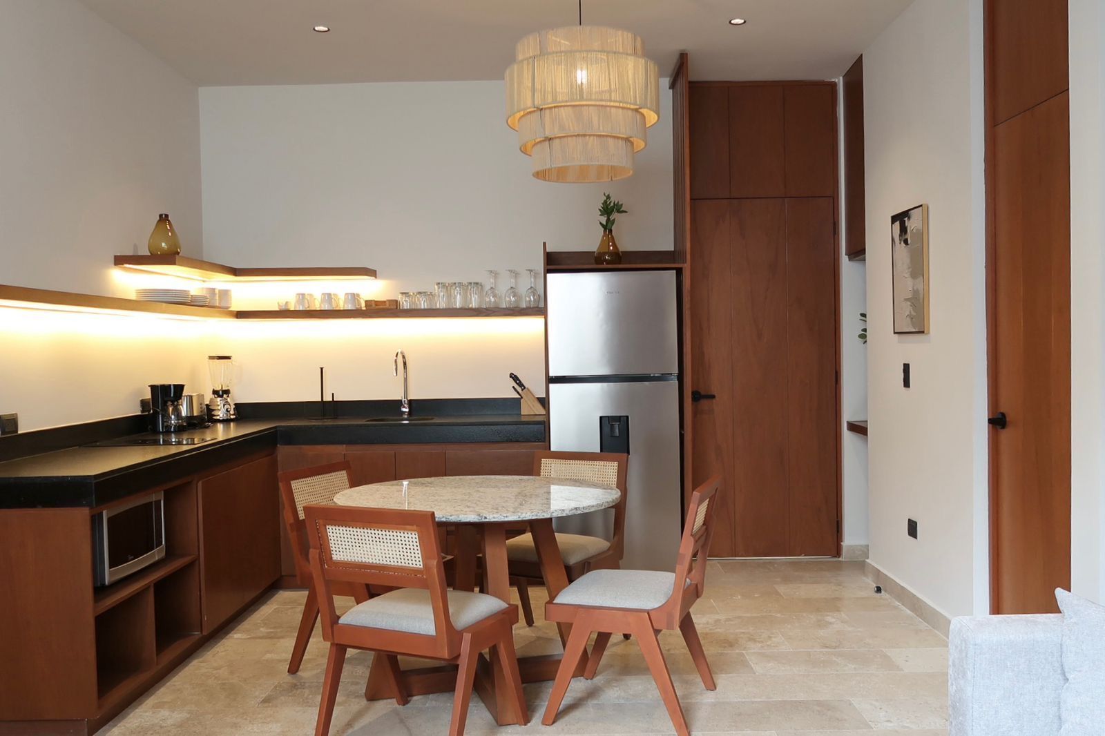Kitchen and dining area with brown cabinets, round table, chandelier, and stainless steel refrigerator.
