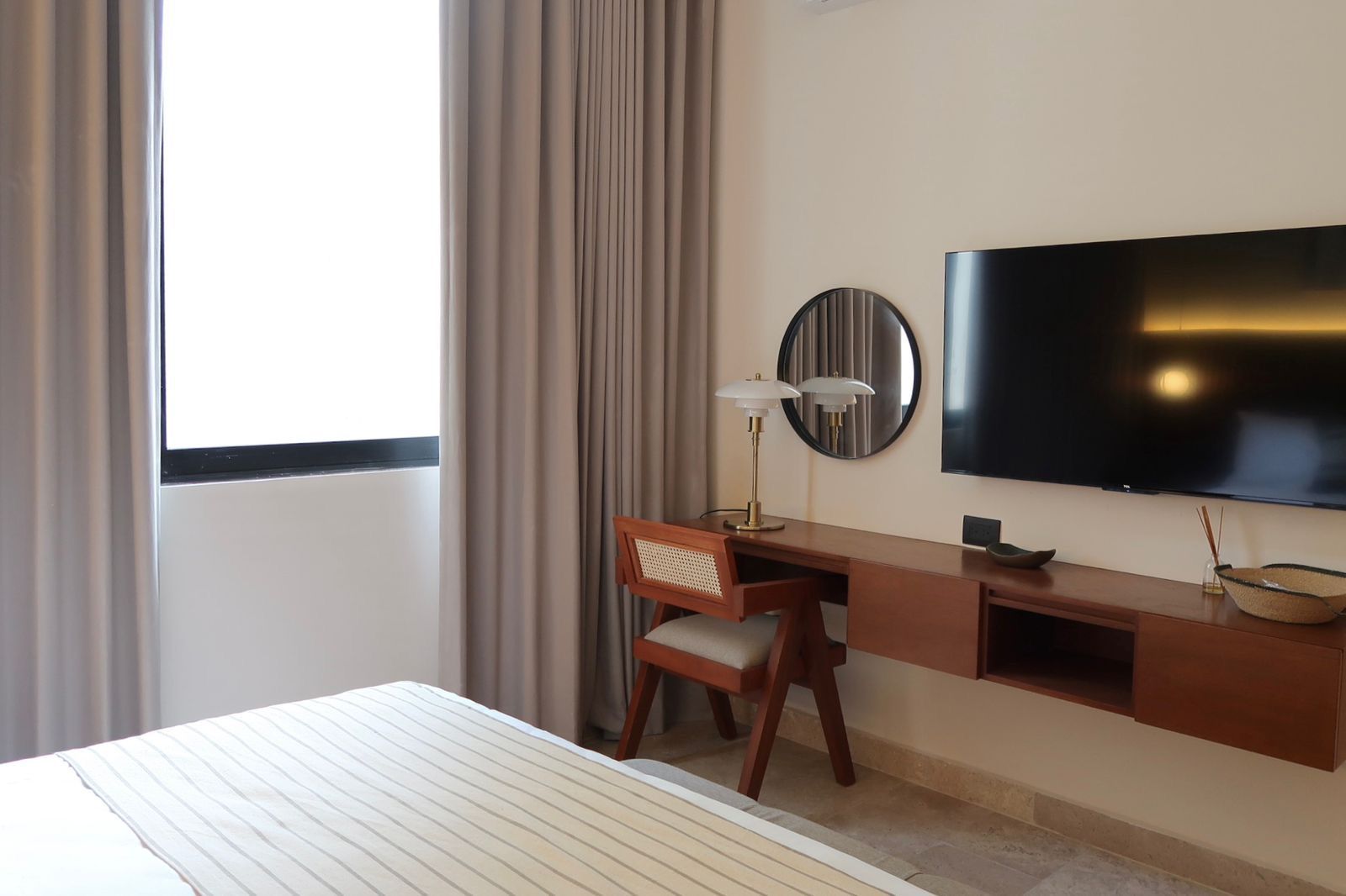 Bedroom with bed, desk, mirror, TV, and window with curtains.