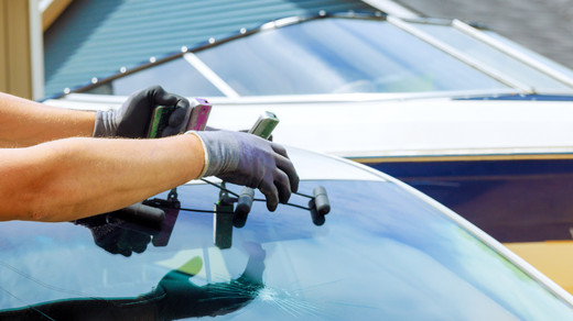 Person with gloved hands repairing a windshield with tools.