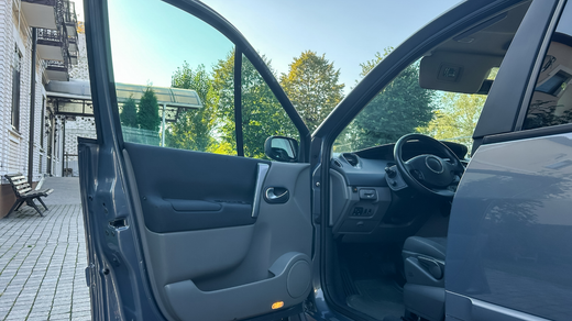 Dark blue car door open, interior visible. Black steering wheel, dashboard, and seat. Bright daylight.