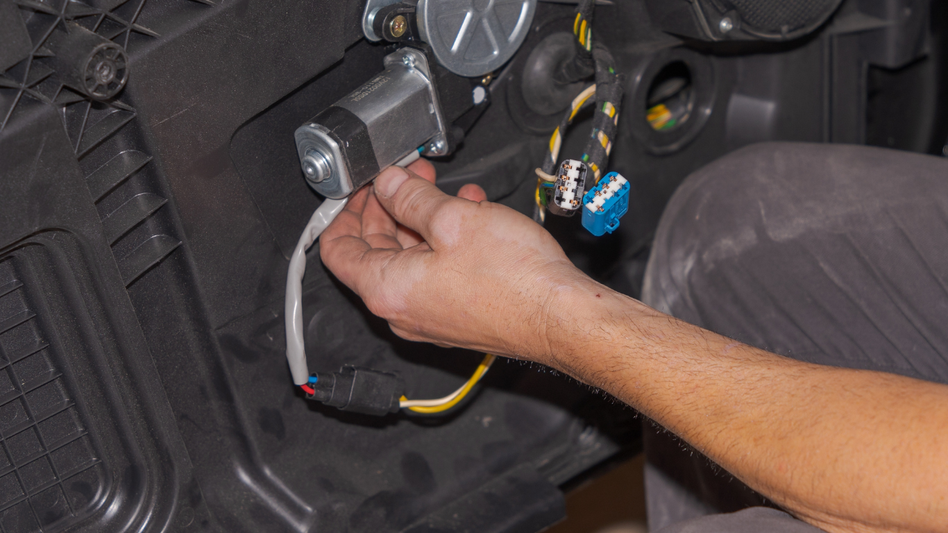 Person connecting wires to a silver window motor in a car door.