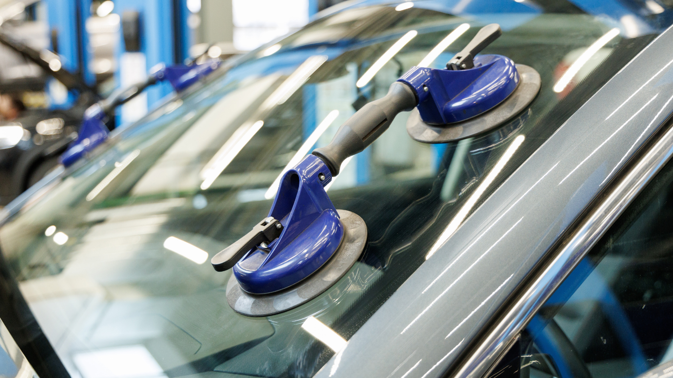 Blue suction cups attached to a car windshield in a repair shop.