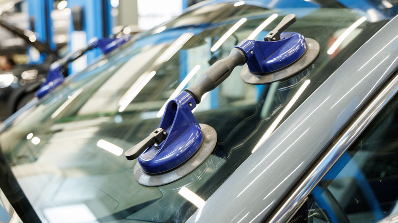 Blue suction cups attached to a car windshield in a repair shop.