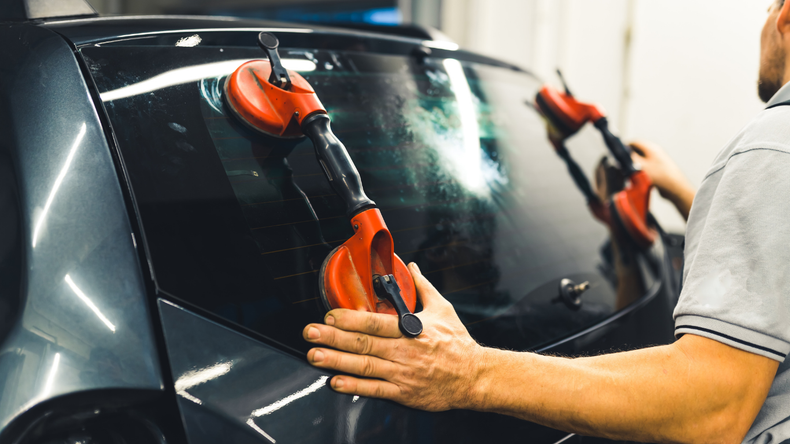 A person using red suction cups to install a dark car window in a repair shop.