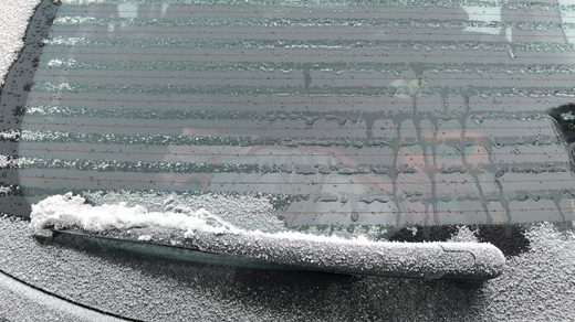 Rear car window covered in frost with a snow-covered wiper blade.