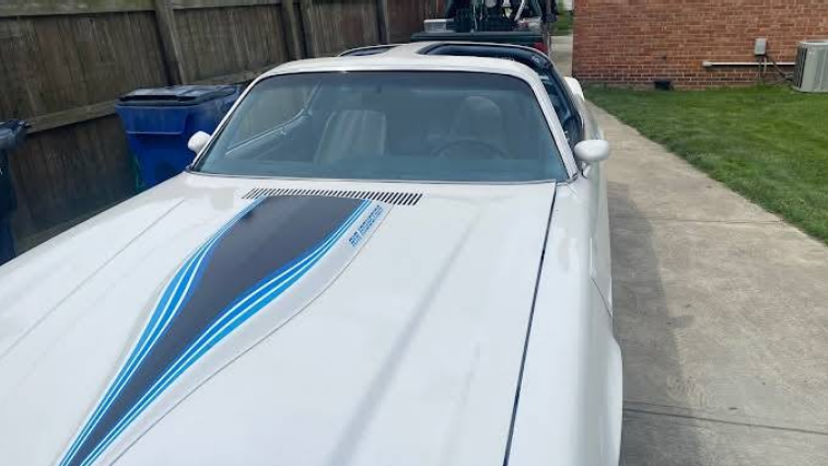 White classic car with blue and black hood stripes parked on a driveway.