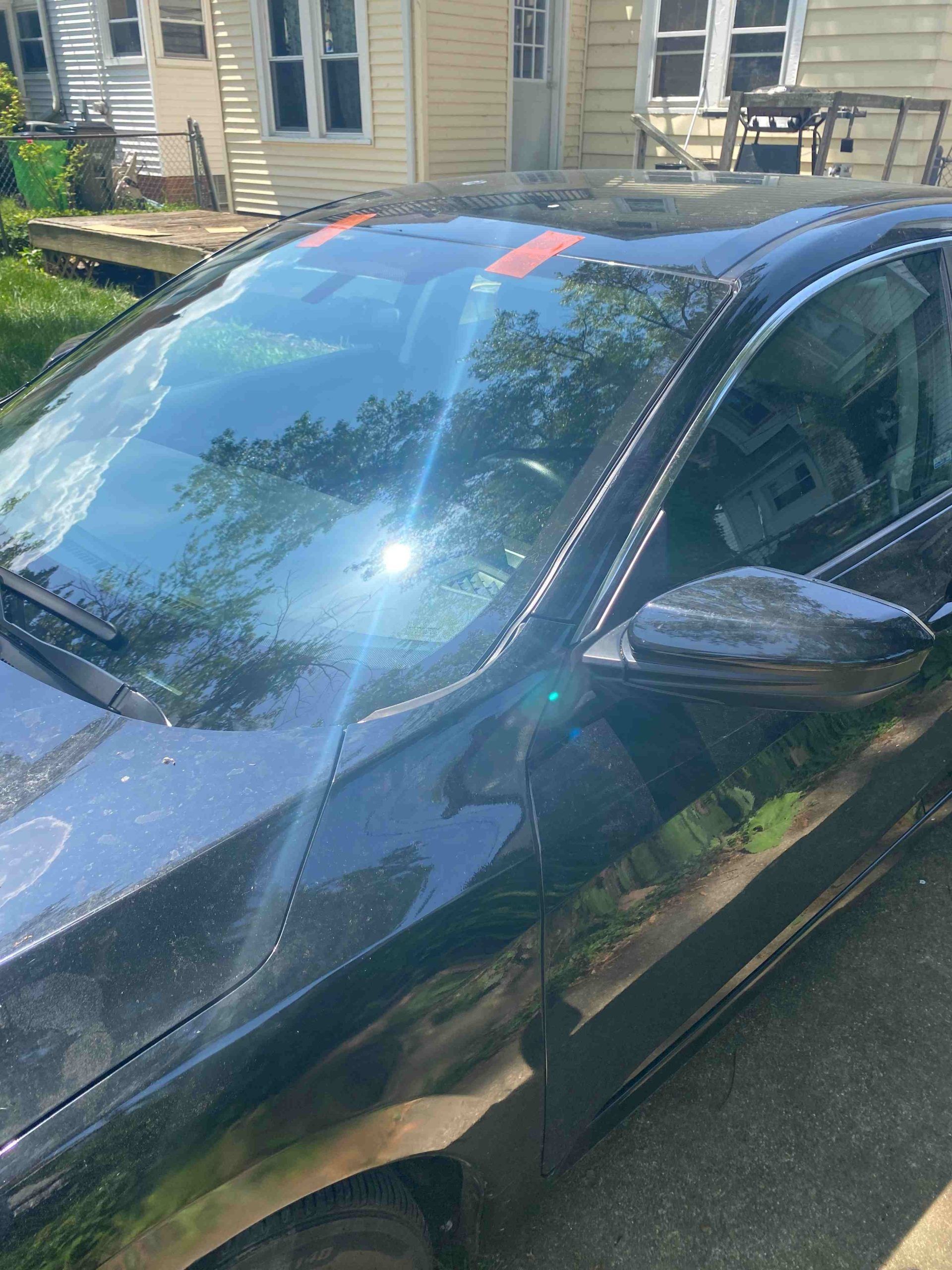 Black car with orange tape on windshield, parked outdoors on a sunny day.