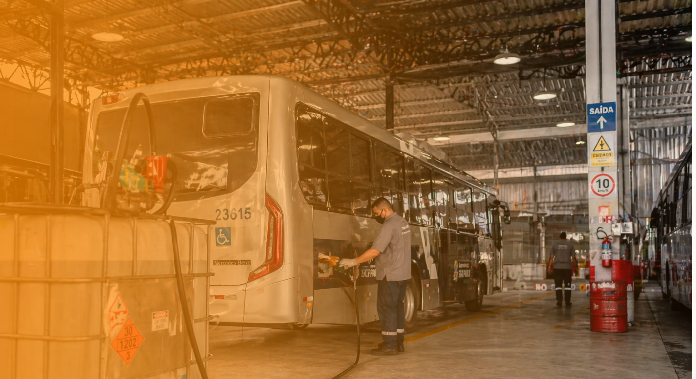 Um ônibus sendo abastecido em uma garagem por um funcionário 