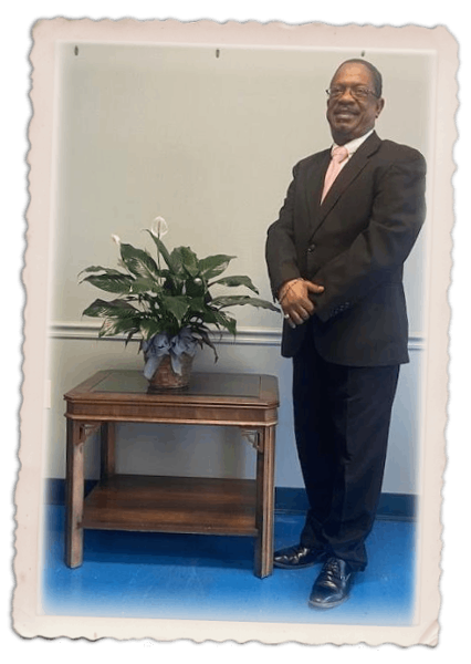 Man in dark suit stands against a purple and gold backdrop.