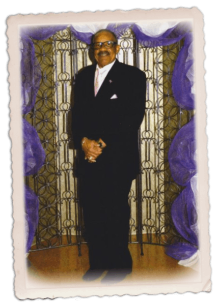 Man in dark suit stands against a purple and gold backdrop.