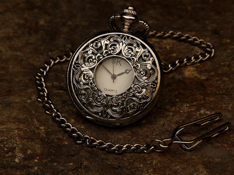 Silver pocket watch with ornate design and chain on a brown stone surface.