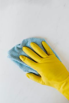 A person wearing yellow rubber gloves is cleaning a white wall with a blue cloth.