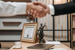 Two men are shaking hands in front of a statue of justice.