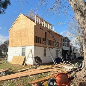 House under construction: adding second story. Workers, wood, ladders, sunny day.