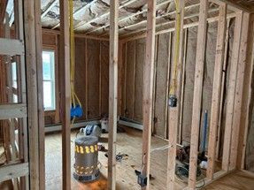 Interior framing of a room under construction, showing studs, insulation, electrical wiring, and a space heater.