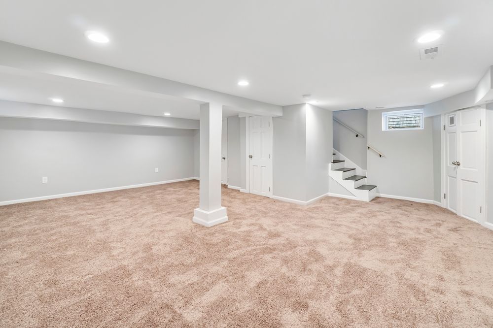 Empty, carpeted basement with white walls, recessed lighting, and a staircase.