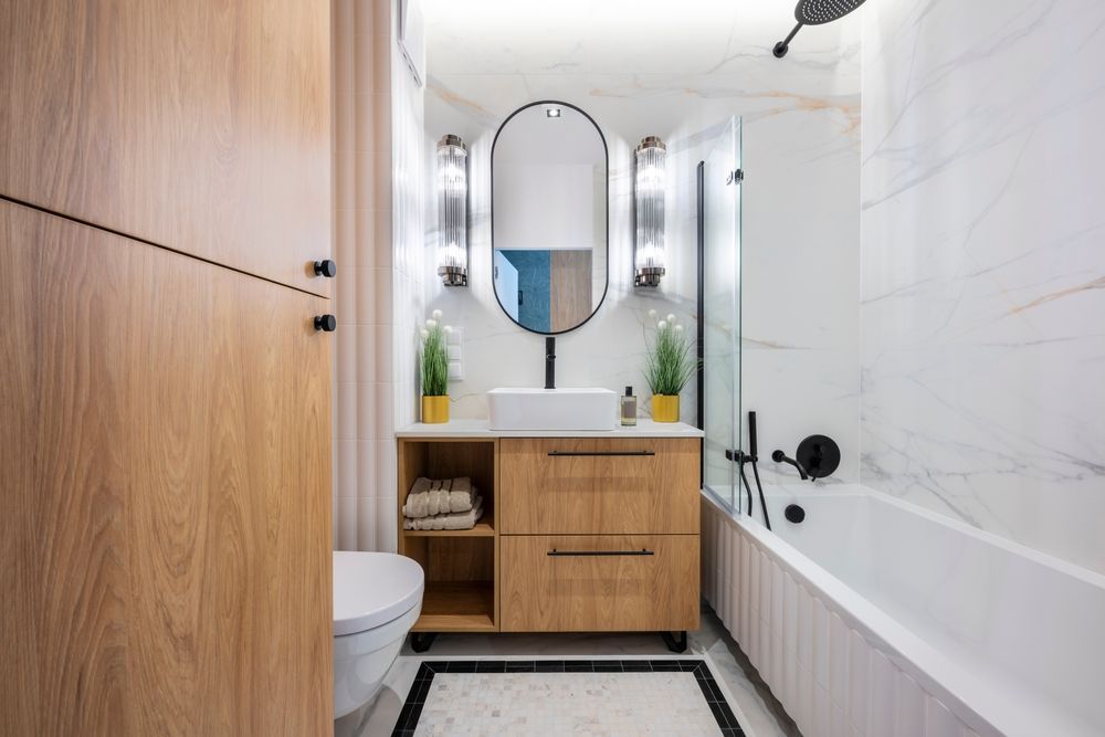 A modern bathroom with wooden cabinets, white sink, and black fixtures.