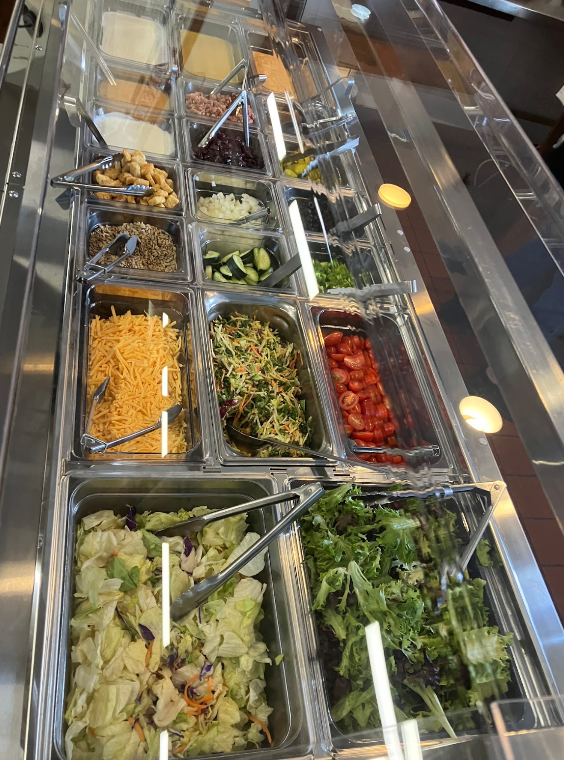 Salad bar with various toppings like cheese, nuts, and vegetables.