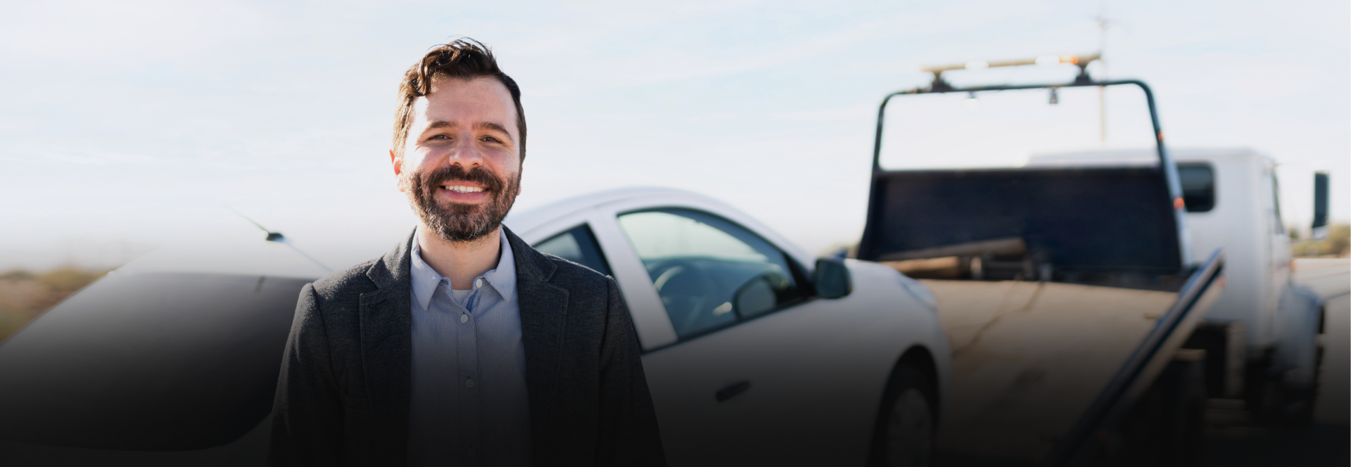 Man smiling next to a car being towed on a sunny day - Snap Towing & Recovery