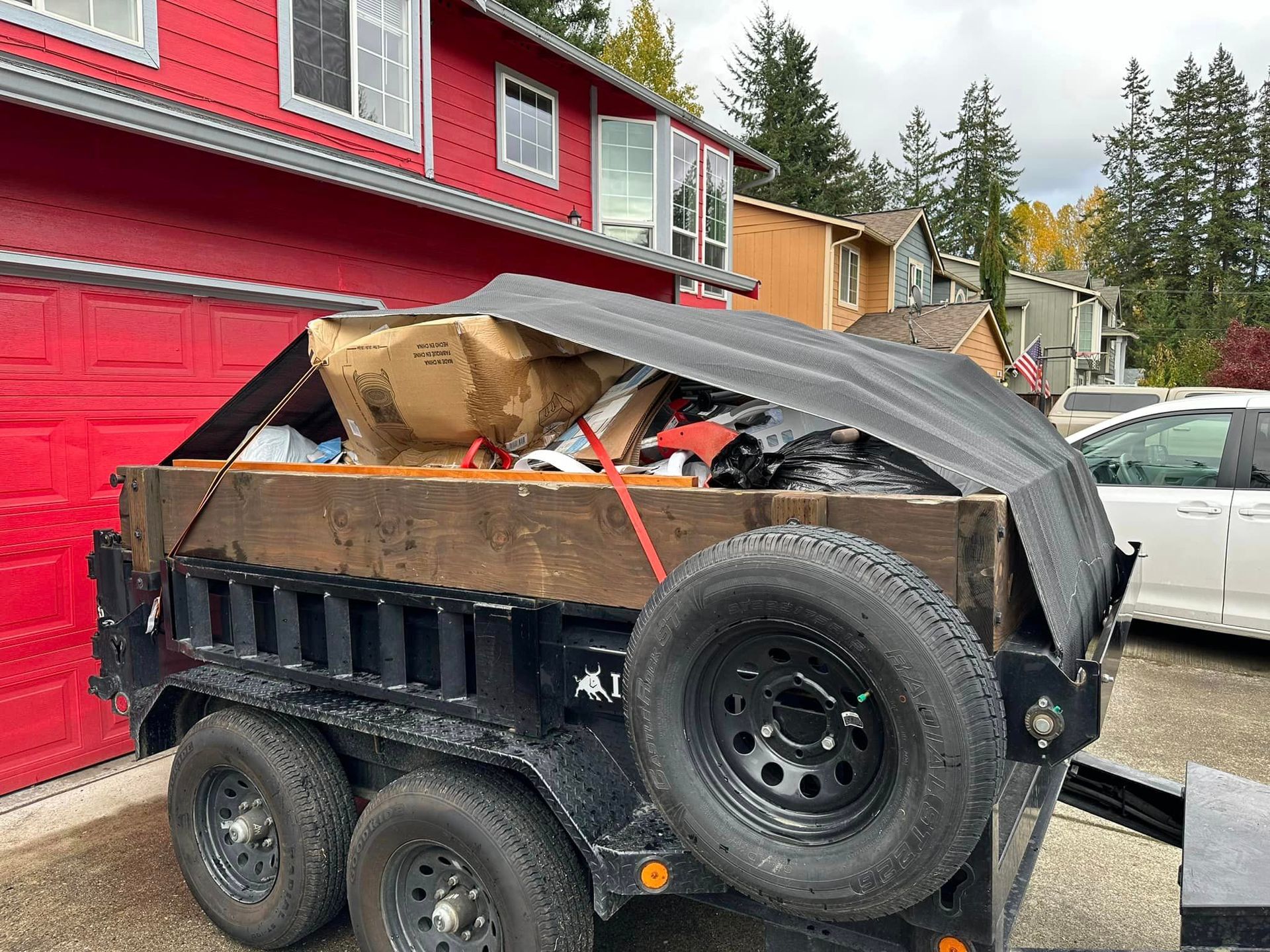 A dumpster trailer filled with trash is parked in front of a red garage door.