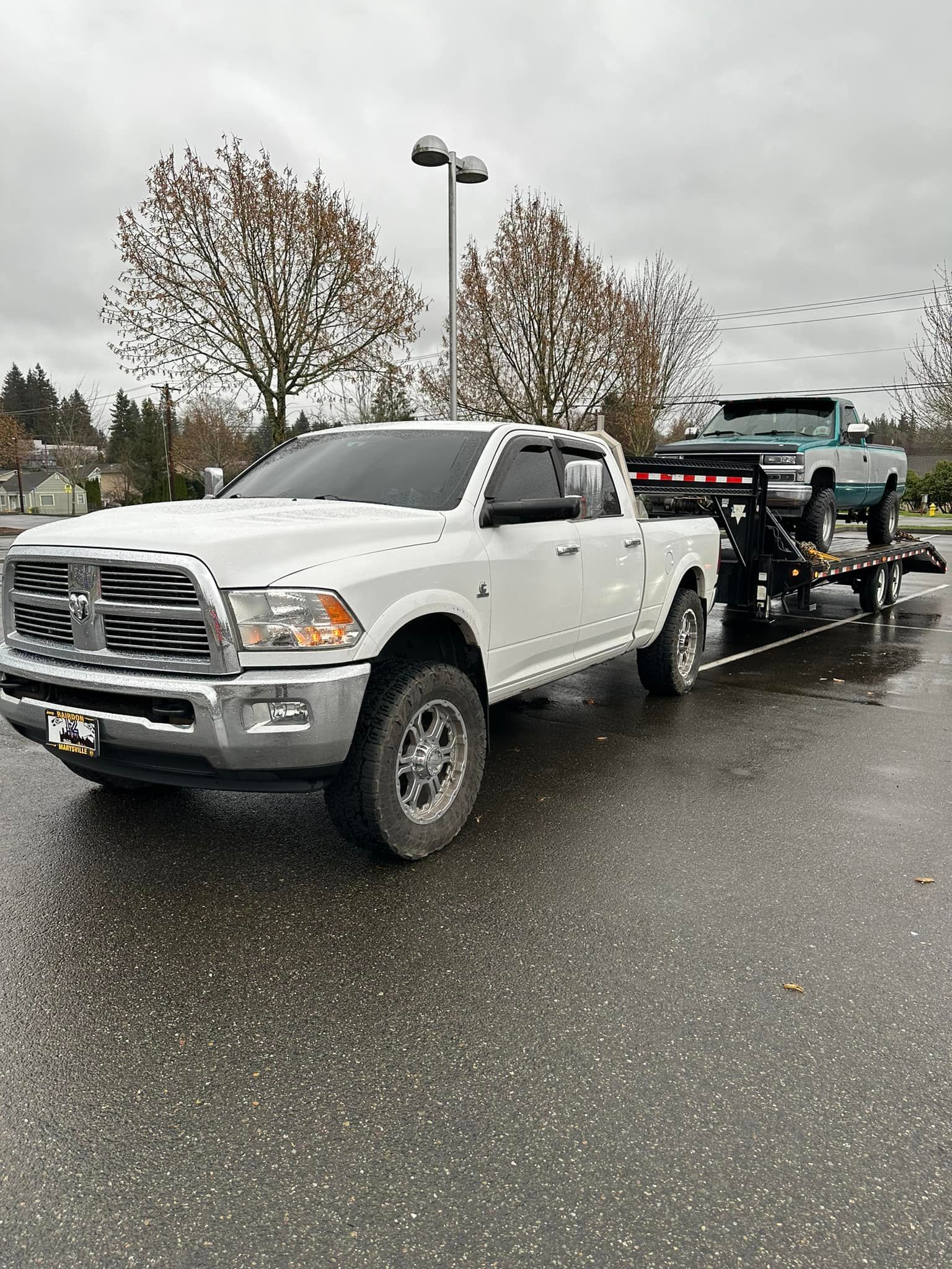 A white truck is towing a trailer with a motorcycle on it.