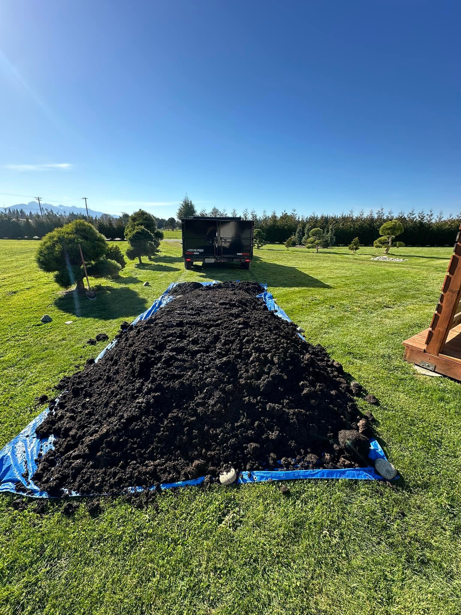 A large pile of dirt is sitting on top of a blue tarp in a grassy field.