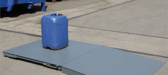 Un contenitore di plastica blu è appoggiato su una rampa di metallo grigio, all'aperto.