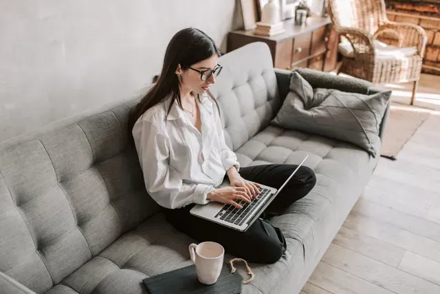 A woman is sitting on a couch using a laptop computer.