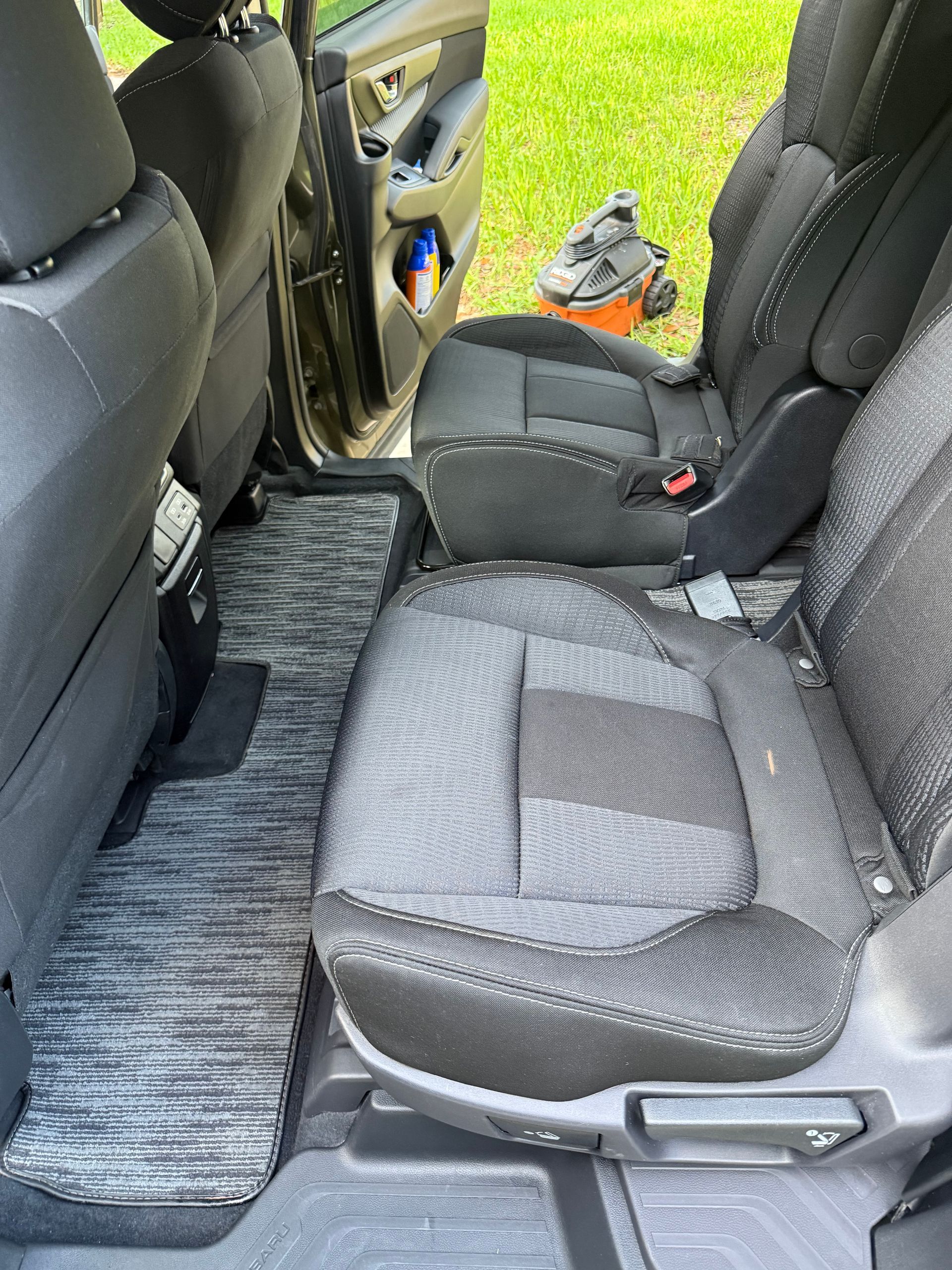Interior car view with open door, showing gray fabric seats, patterned floor mat.