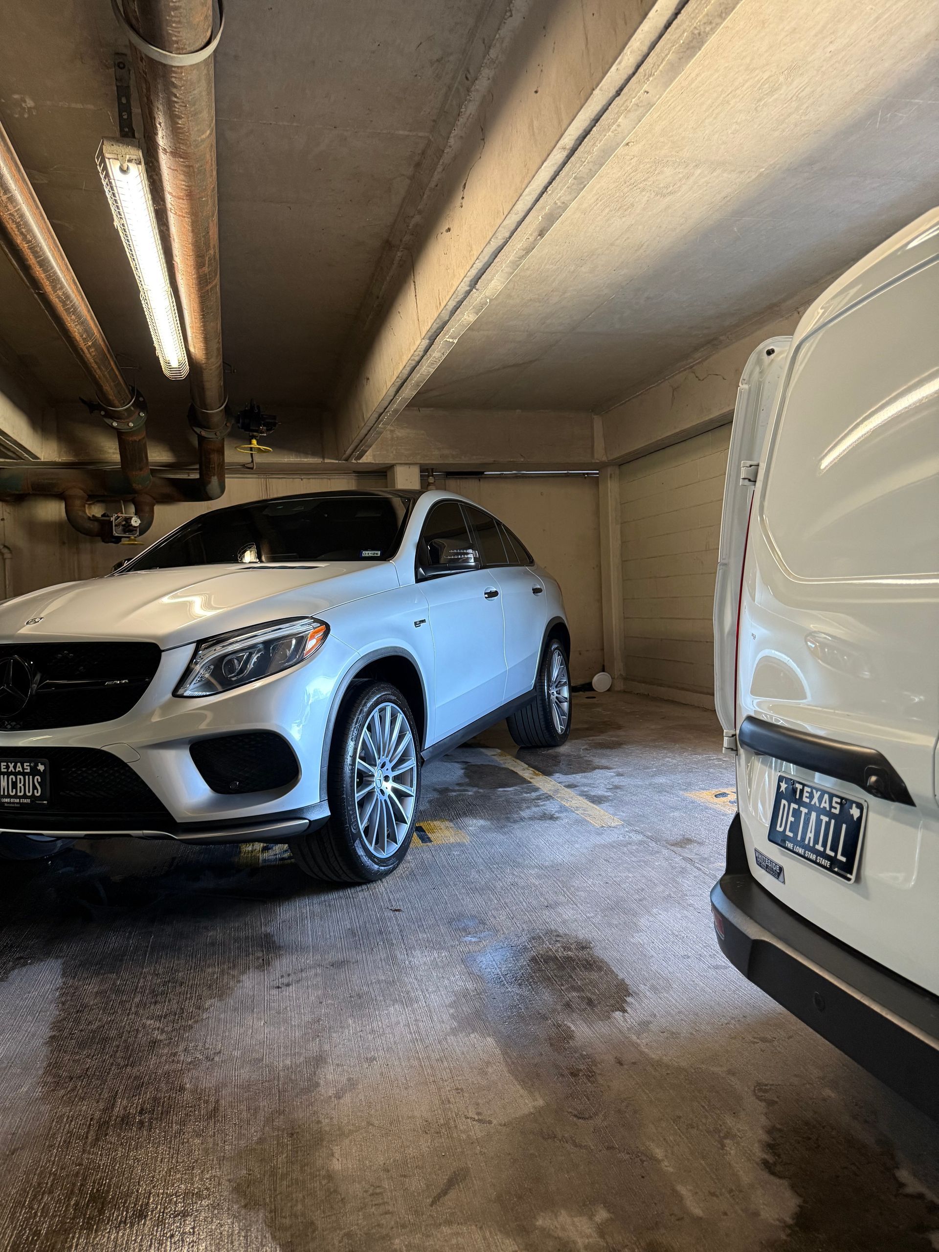 White Mercedes SUV and a white van parked in an underground garage.