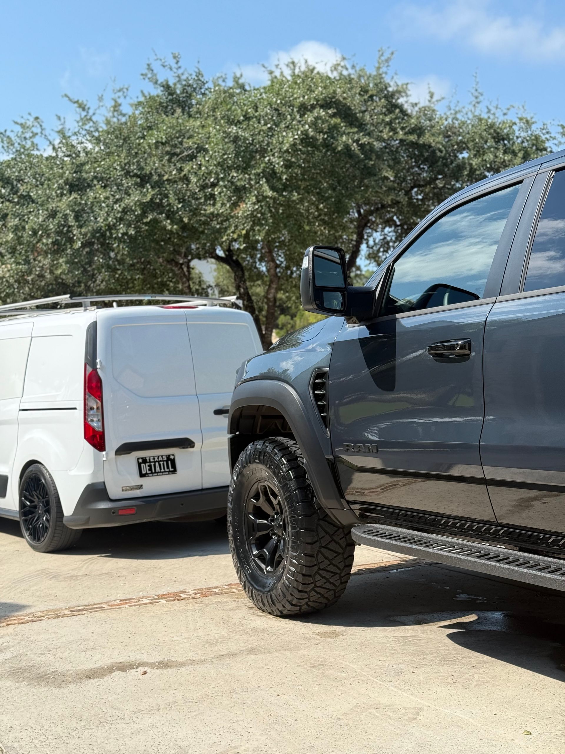 A gray truck with black wheels next to a white van on a sunny day.
