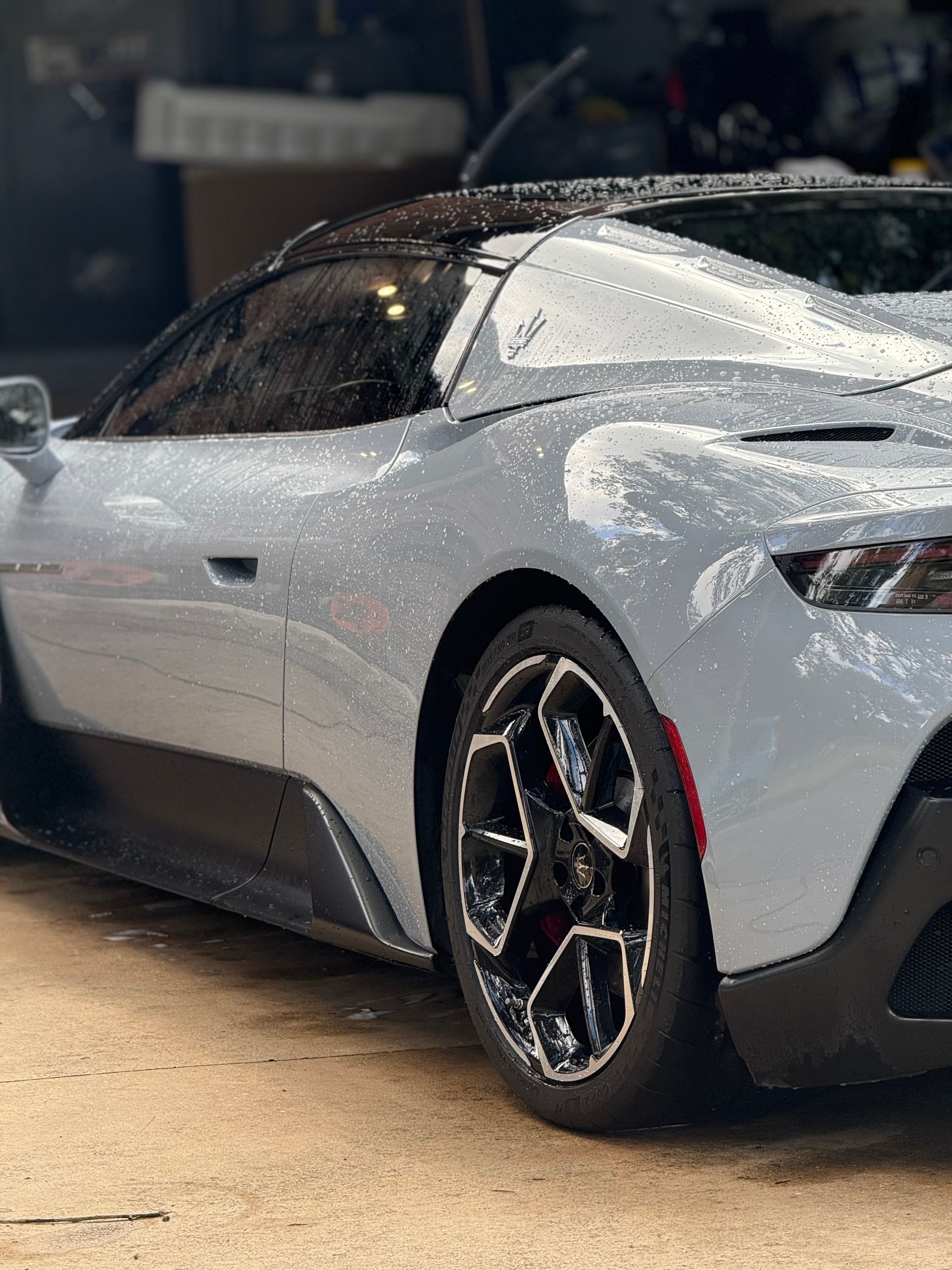 Gray sports car, wet with raindrops, parked outdoors.