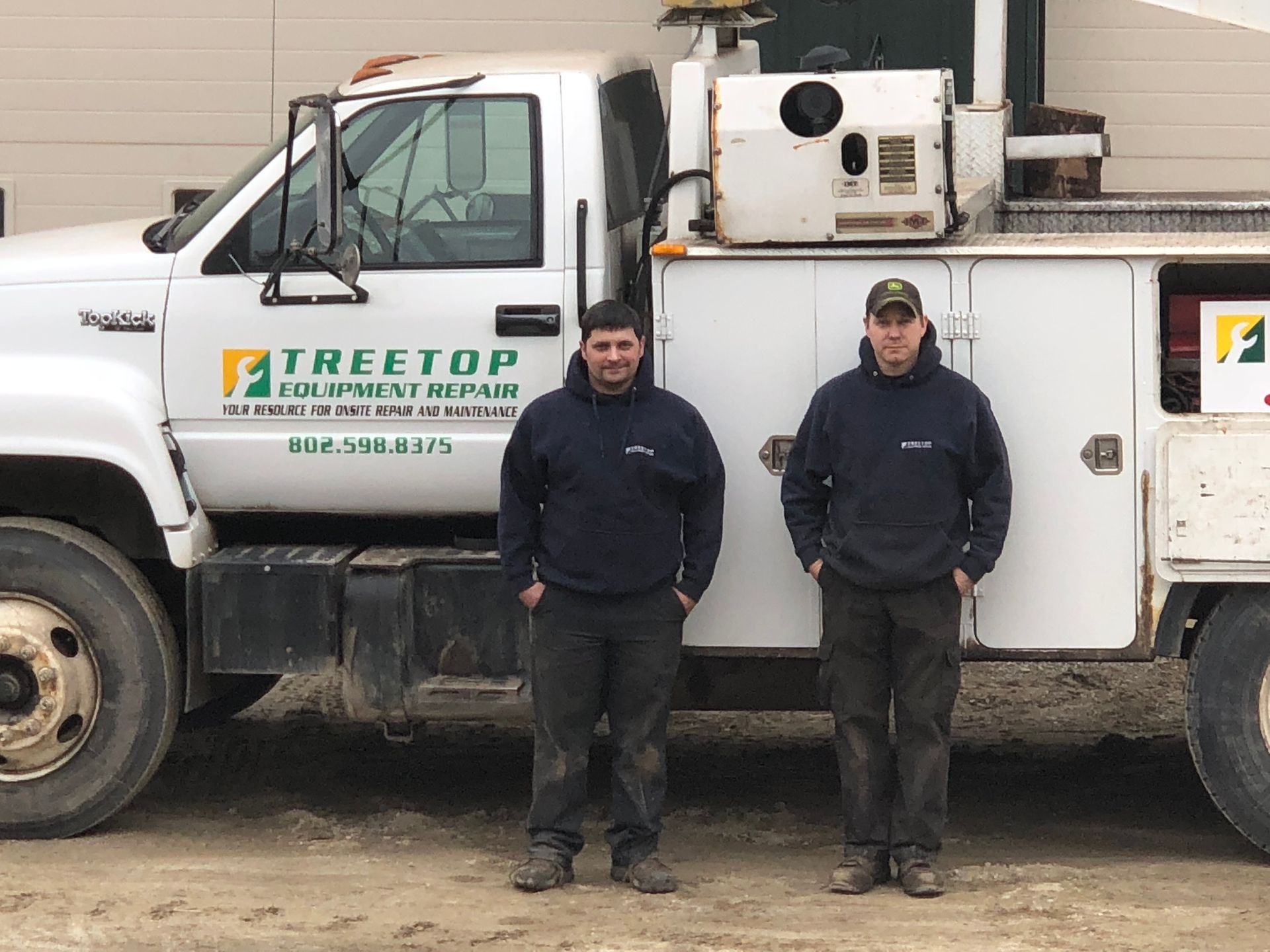 Two men are standing in front of a treetop utility truck