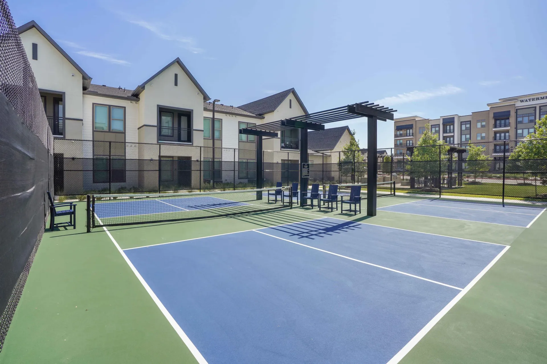 Outdoor community tennis court with net and seating, surrounded by apartment buildings.