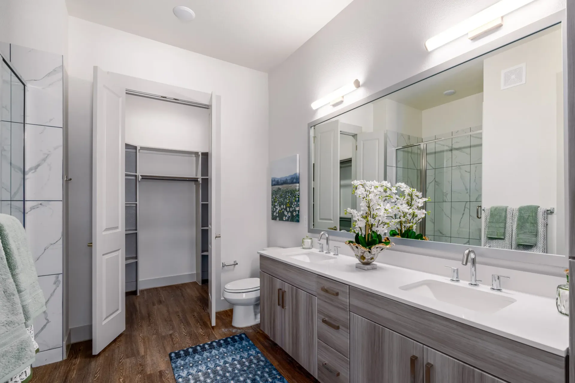 Modern apartment bathroom with double sink vanity, large mirror, and walk-in closet.