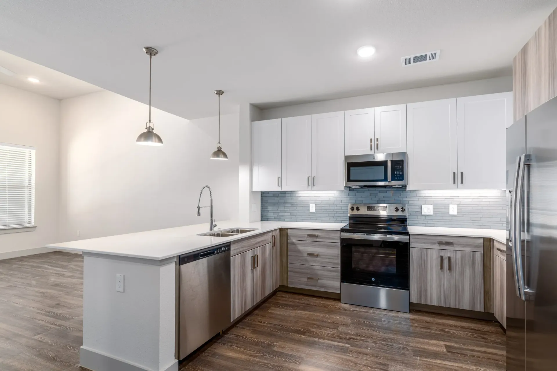 Modern kitchen in an apartment with white upper cabinets, gray lower cabinets, an island, and stainless steel appliances.