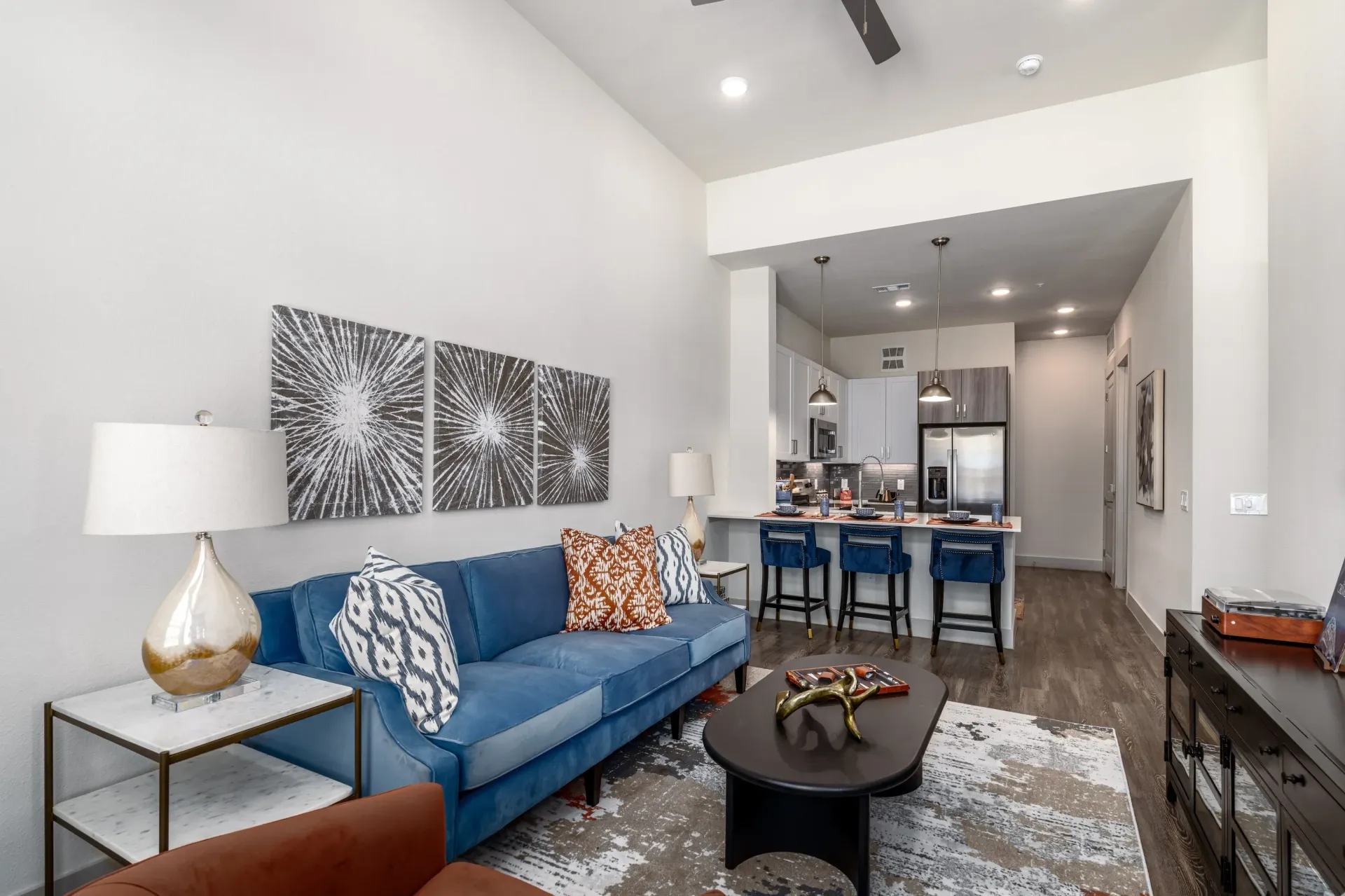 Open-concept living area with blue sofa, coffee table, and bar-height kitchen with four stools.