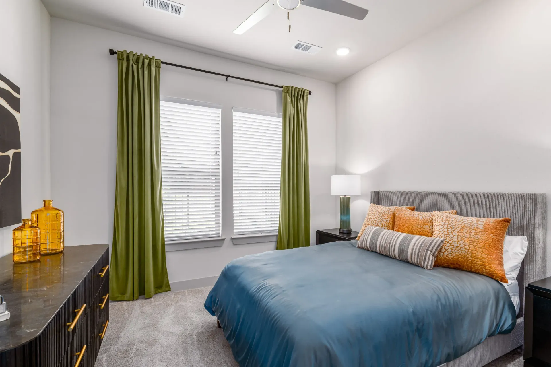 Bedroom with blue comforter, gray upholstered bed, and green curtains.