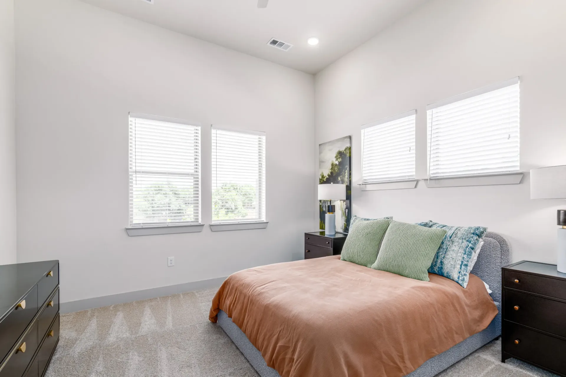 Bedroom in a modern apartment with a bed, two nightstands, and blinds on multiple windows.