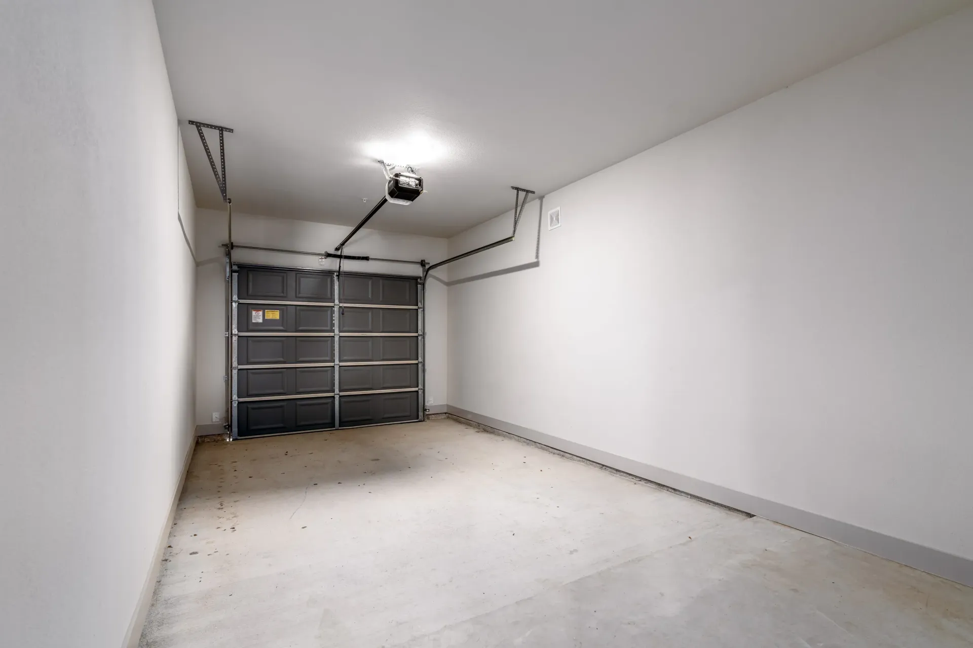 Empty residential garage with a dark sectional door, concrete floor, and white walls.
