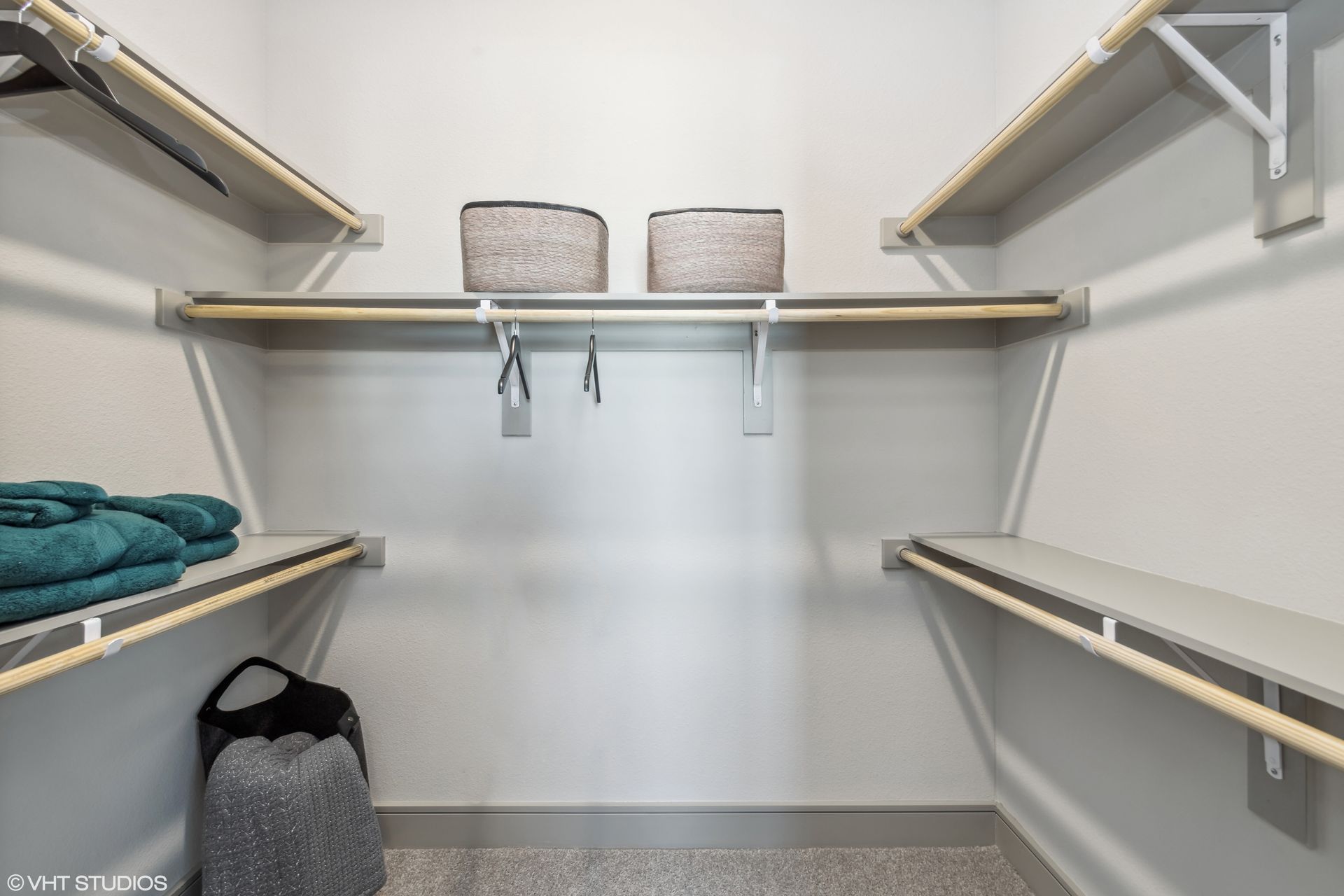 Empty walk-in closet with white shelves, hanging rods, and two gray storage bins on the top shelf