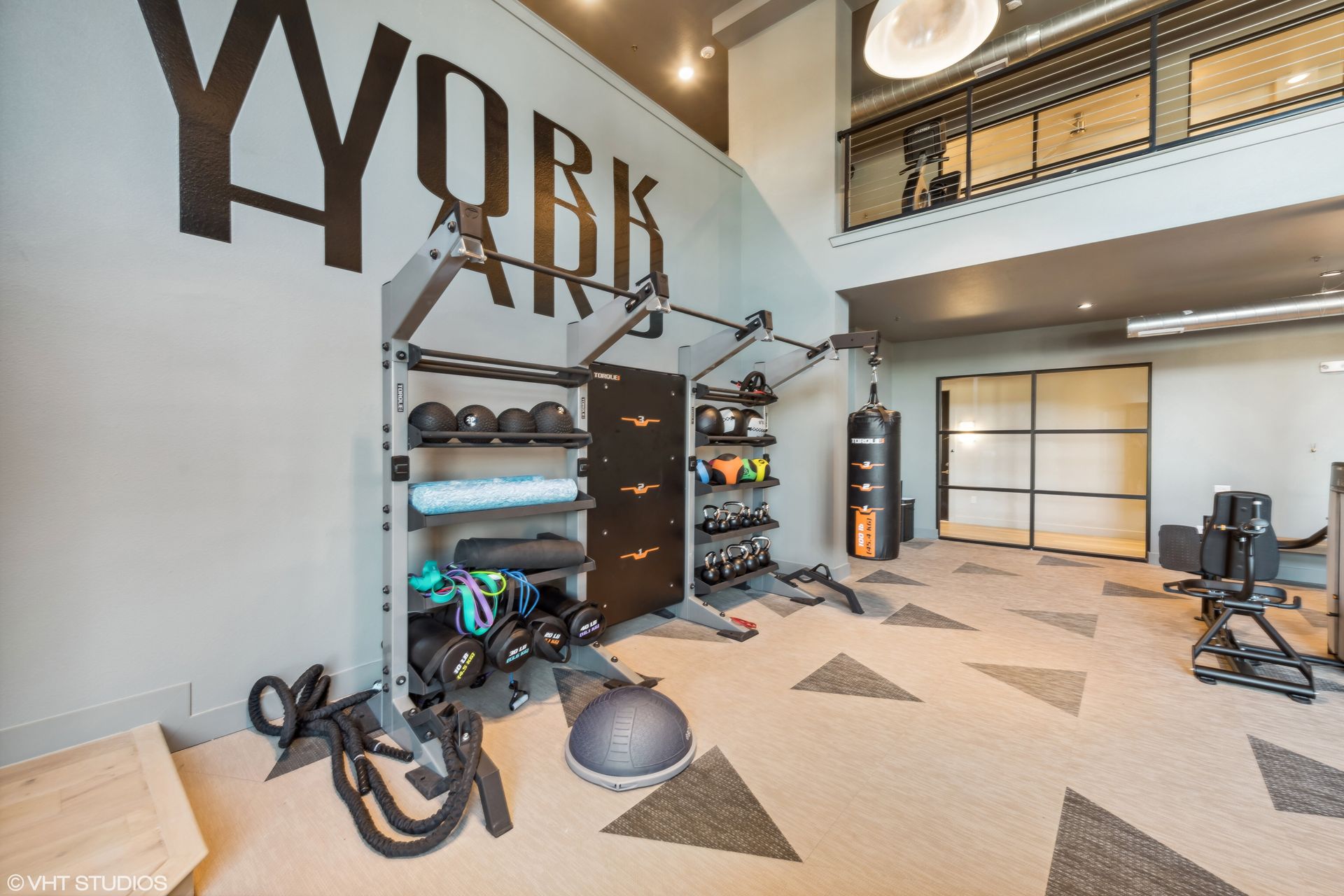 Modern gym room with weights, exercise machines, and a large wall logo in a bright loft space