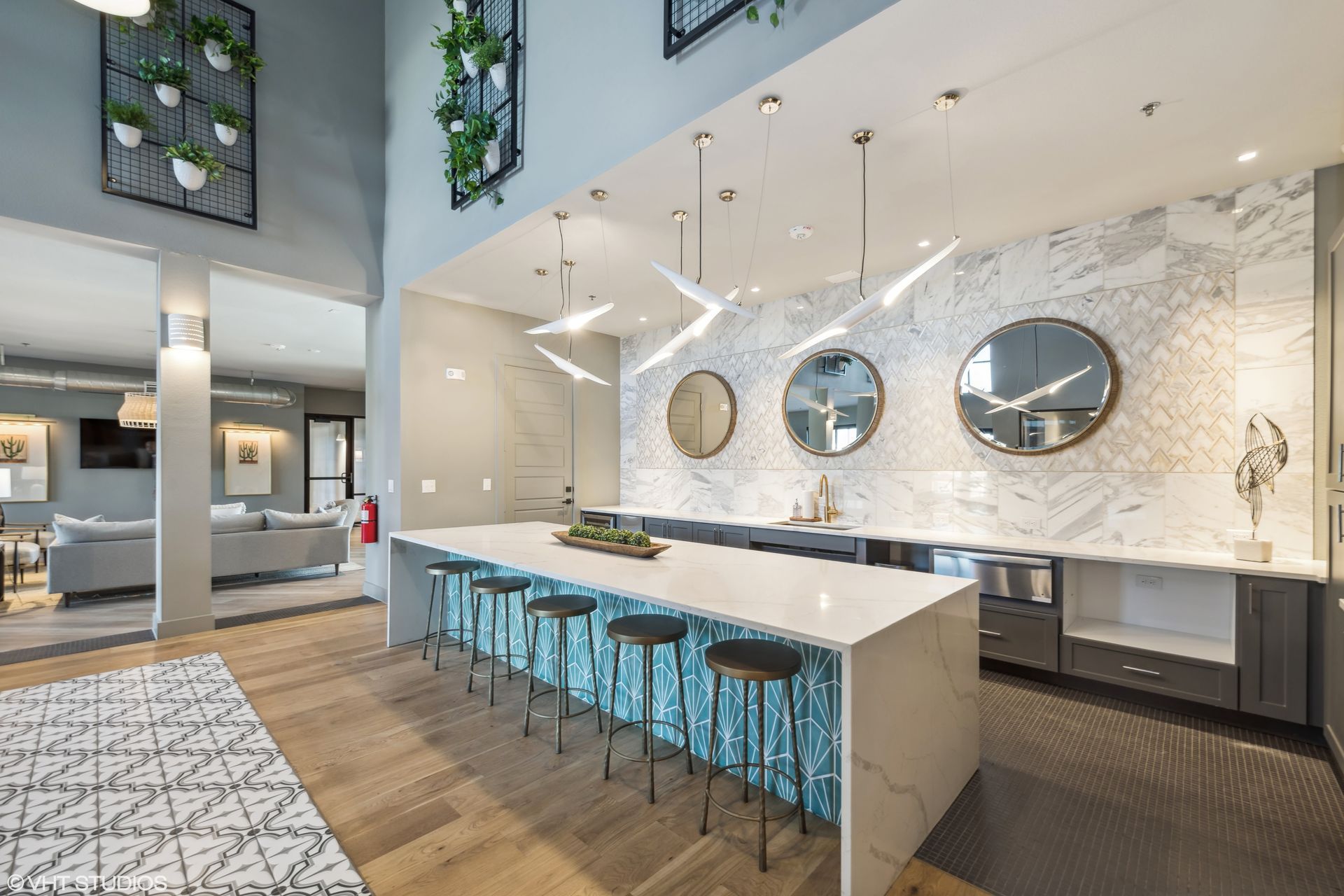 Modern kitchen with a large island, teal stools, marble backsplash, and pendant lighting in a bright open space