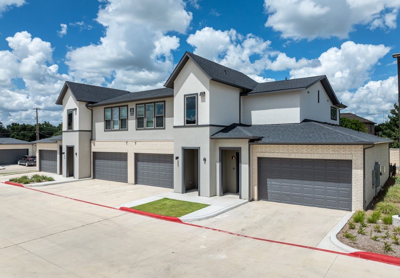 Modern two-story townhouses with gray garages and white siding under a bright blue sky