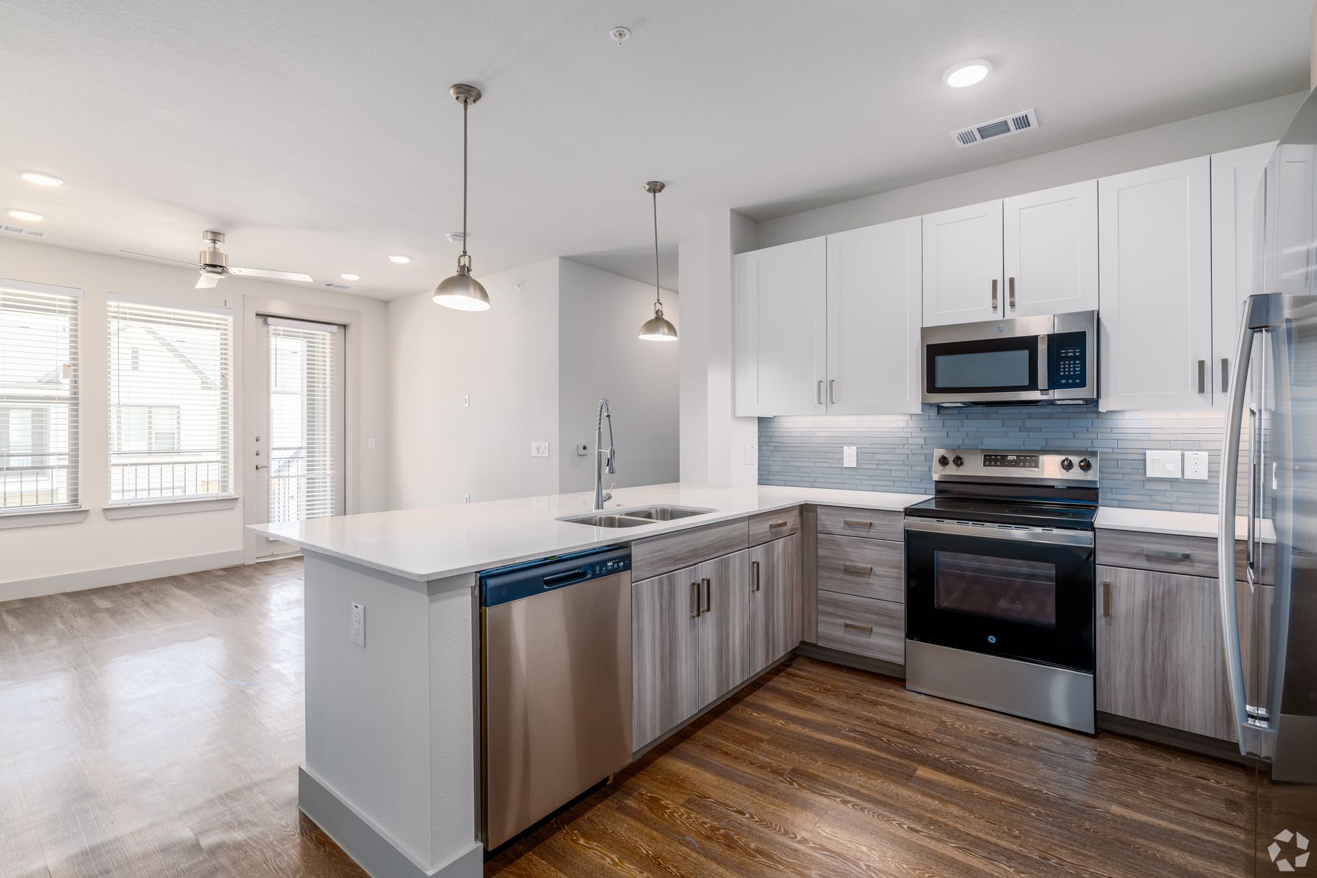 Modern white kitchen with stainless appliances, island, pendant lights, and open living area with hardwood floors