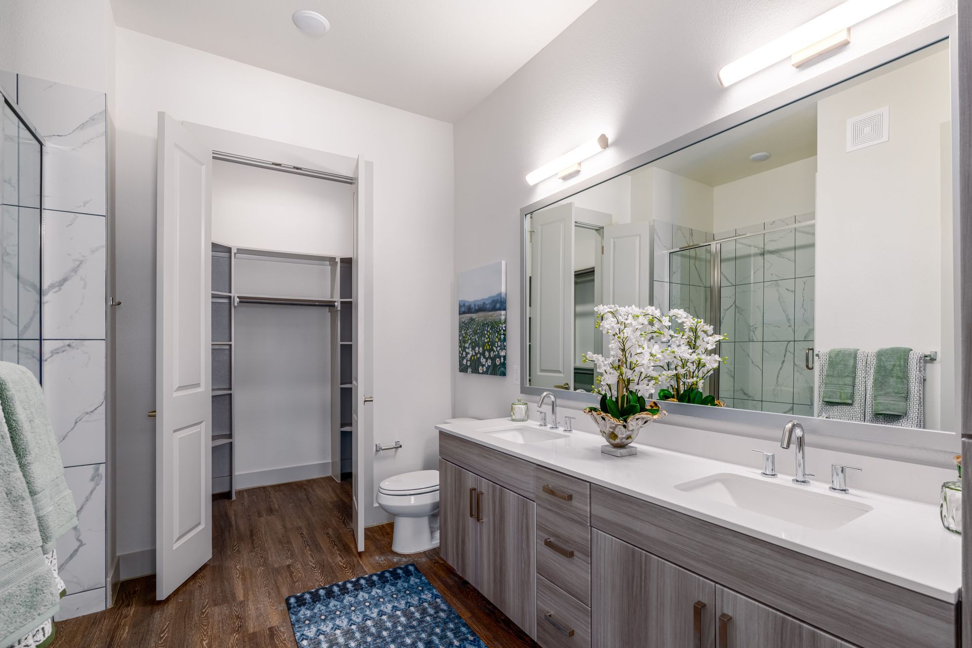 Modern bathroom with double vanity, large mirror, white orchids, and open closet area