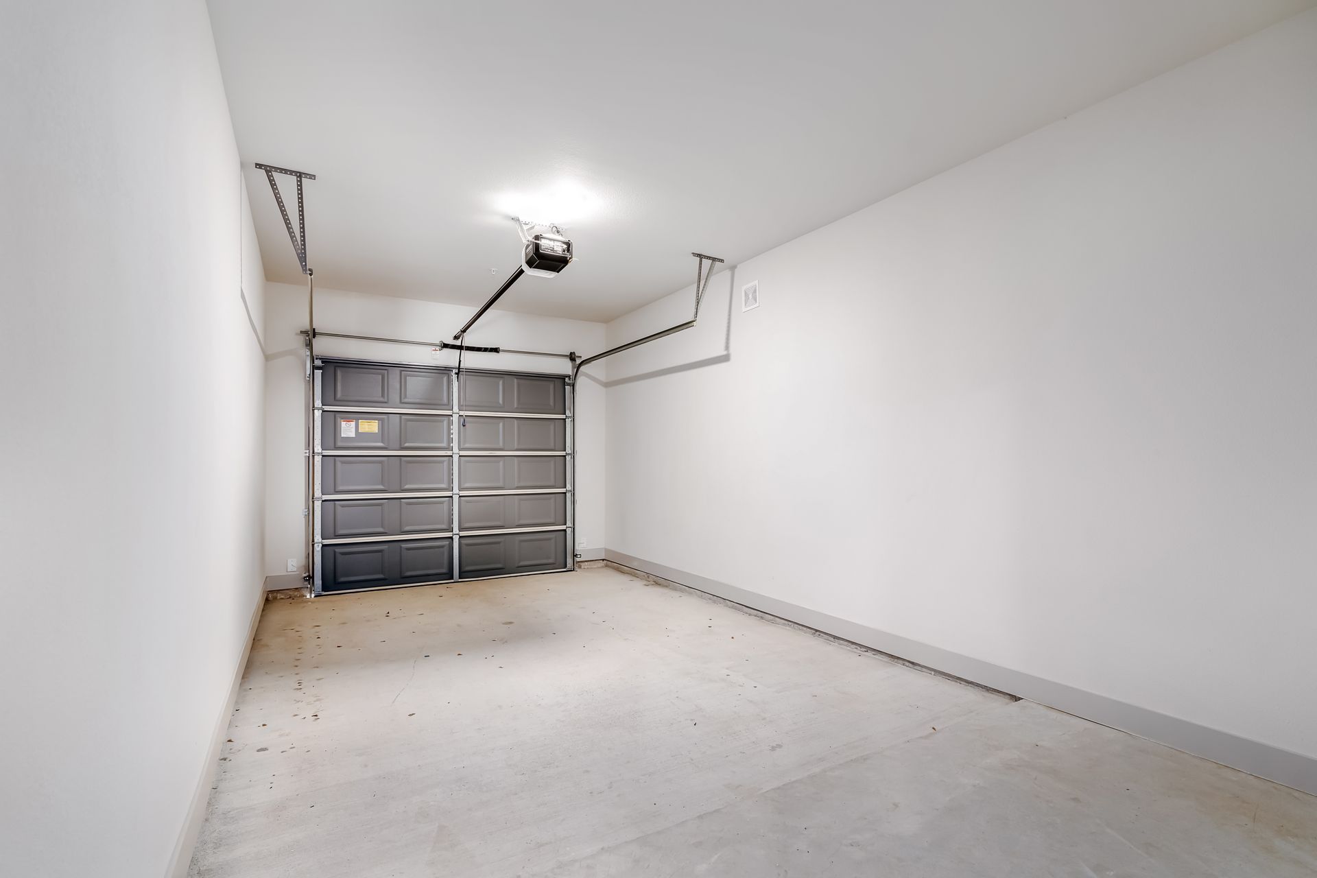 Empty white garage interior with closed gray double door and overhead opener